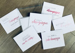 Six white champagne-inspired notecards with a mix of ombre pink script text and gray block type. Champagne Lovers collection by Stationare.