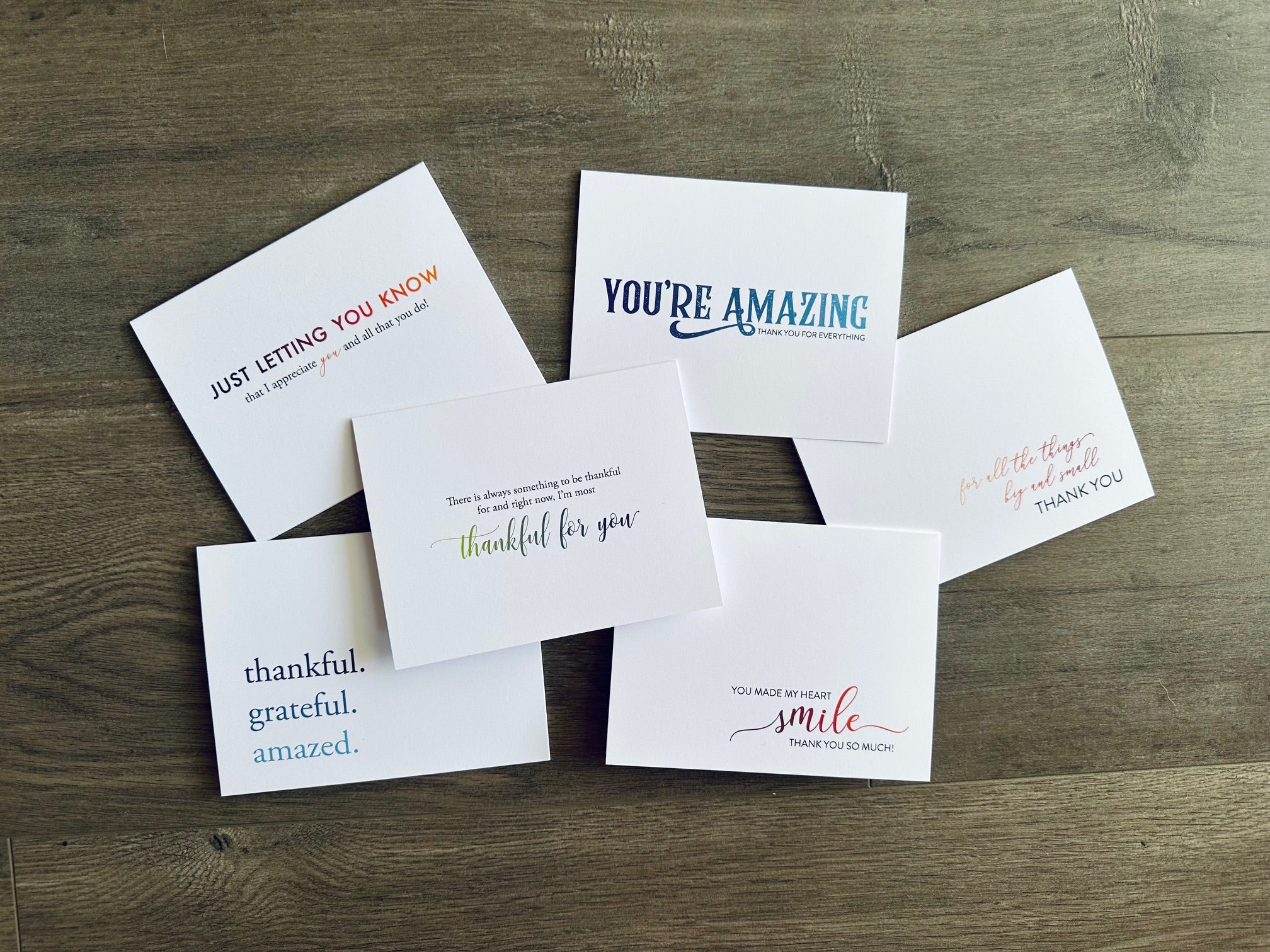 Set of 6 white notecards lie on a wooden background. Each card has a sentiment expressing gratitude.