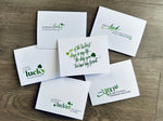 Six white Irish-themed notecards lie on a wooden background. Each card has a mix of fonts in differing greens and share a friendship-themed saying about luck.