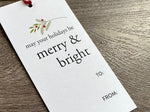 White Chistmas gift tag with 'may your holidays be merry & bright' text on a wooden surface