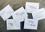 Six white travel-themed notecards are overlapping on a wooden background. Each card has a mix of fonts and colors with a quote encouraging or expressing love for traveling. Travel Lovers Collection by Stationare.