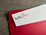 A closeup image of white notecard angled inside a bold red envelope. The closeup shows that the card is slightly textured and says "hello, love" in the upper left hand corner. By Stationare.