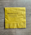 A golden yellow cocktail napkin with gold foil printing that reads: Charcuterie Boards: Where self-control and good intentions go to die. By Stationare.