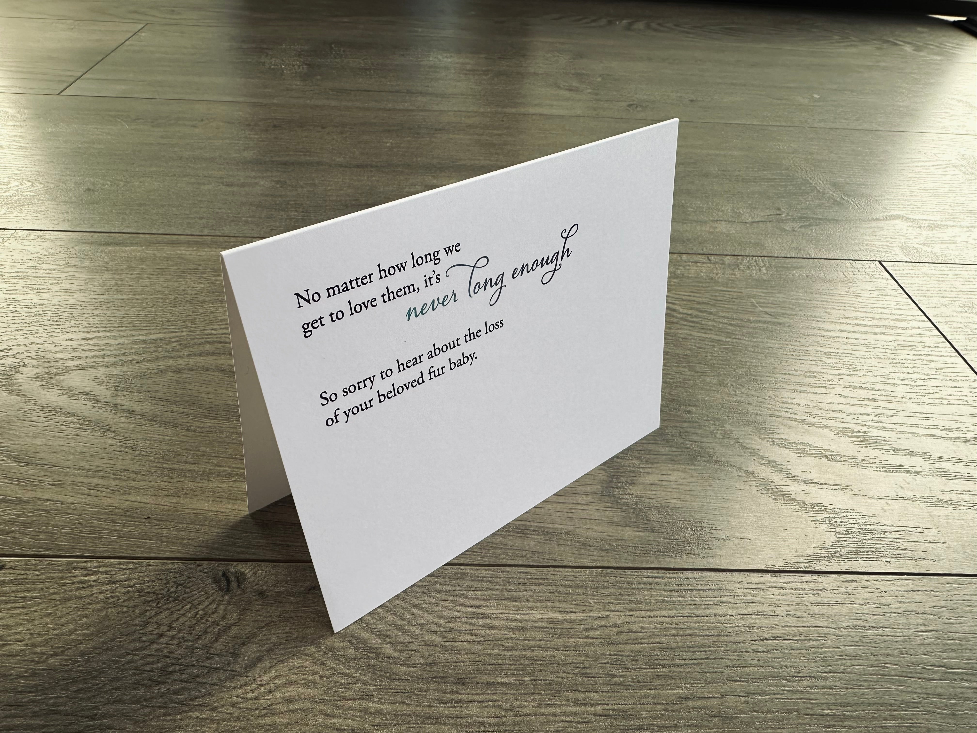 A folded white notecard is propped up and says, "No matter how long we get to love them, it's never long enough. So sorry to hear about the loss of your beloved fur baby." on the front. Loss of Pet by Stationare.