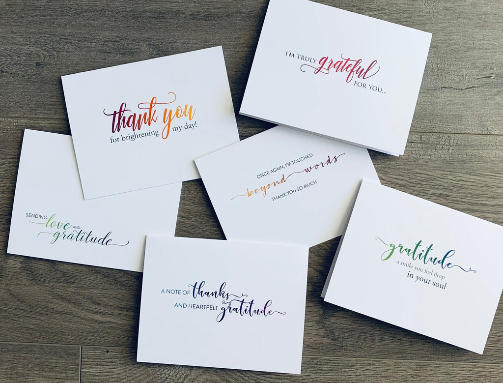 Six white thank you notes are overlapping on a wooden background. Each card has a simple but meaningful thank you sentiment in a mix of fonts and colors. Simply Thanks Collection by Stationare.