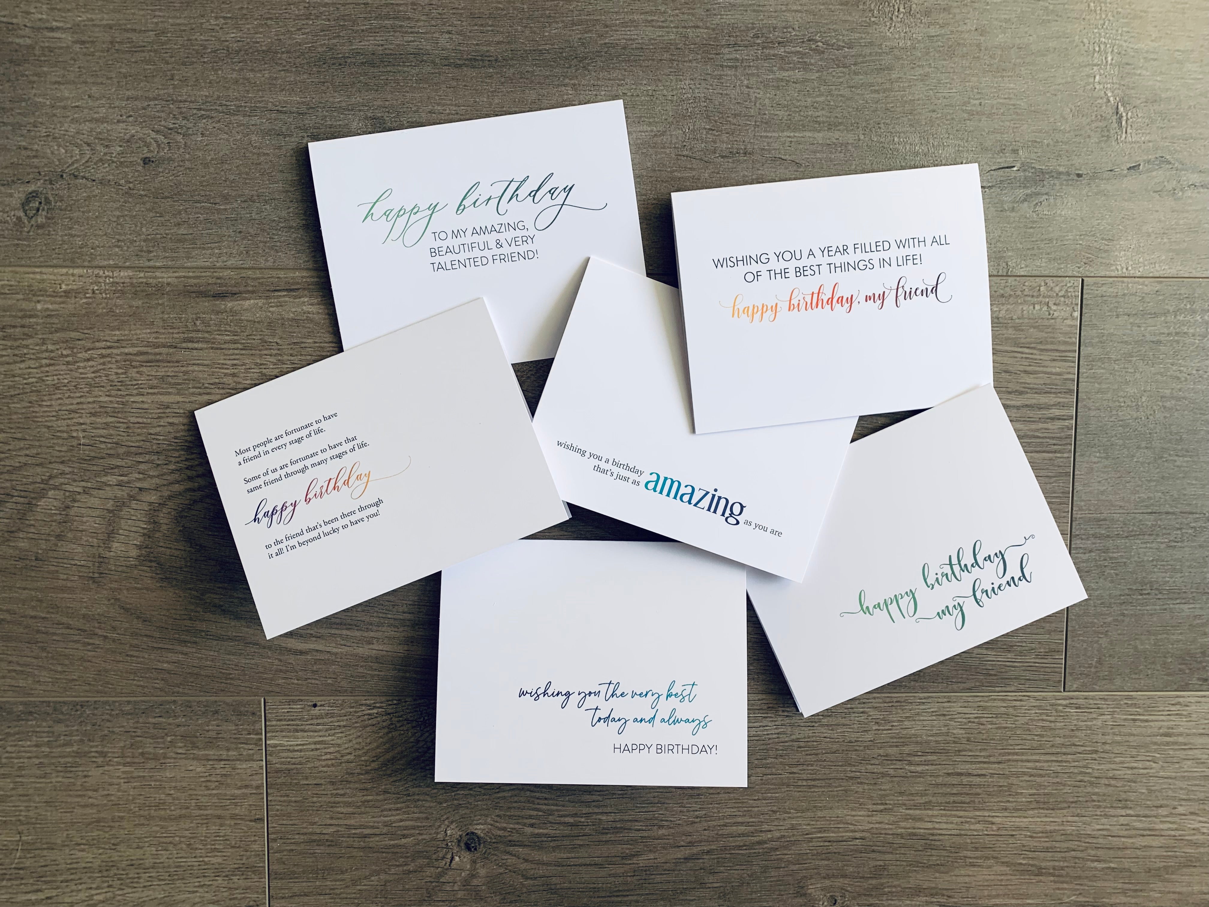 Six white notecards lie on a gray wooden background. Each card has a friendship-inspired birthday sentiment. Friendship Birthday collection by Stationare.