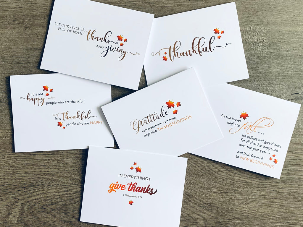 Collage image of 6 white notecards on a gray wooden background. Each card has brown, orange and red font types expressing fall-inspired thanks. Giving Thanks Collection by Stationare