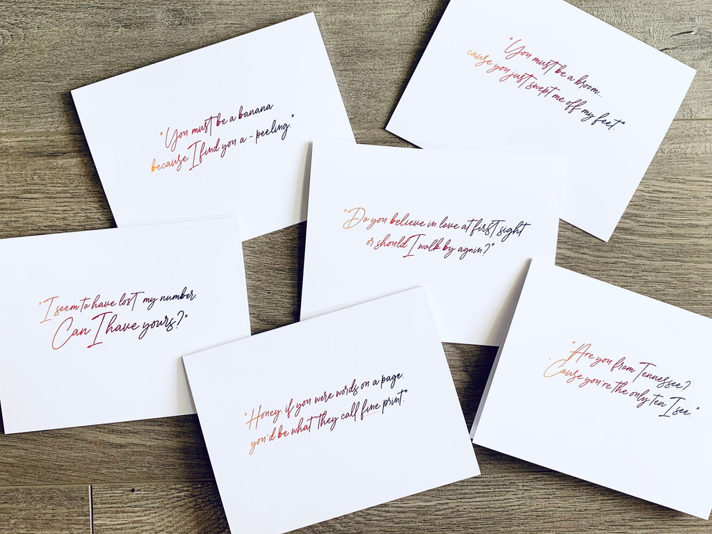 Six white notecards from Stationare's Pickup Lines collection are overlapping on a wooden floor. Each card has a script quote with a funny pick-up line.