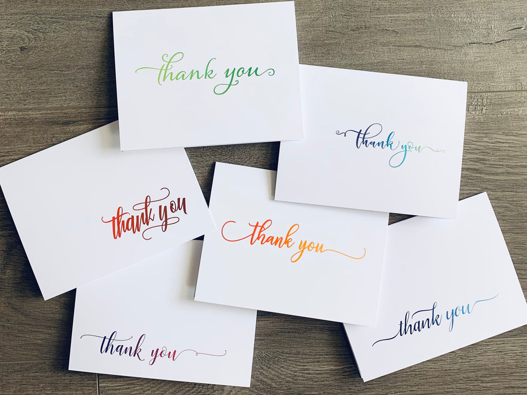 The six cards of Stationare's Thank you collection are overlapped on a wooden floor. Each card has a simple "thank you" in script writing on the front.