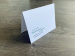 A white notecard is propped up on a gray wooden floor. The card reads, "Thinking of you during this challenging time." Thinking of You collection by Stationare.