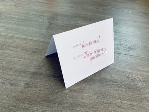 A white card is propped on a gray wood floor. The card reads, "Answer: brownies! Question: There was a question?" Bakers Collection by Stationare.
