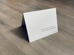 A white, folded notecard sits on a wooden floor. The card says, "The best therapist I know has fur and four legs." Dog Lovers collection by Stationare.