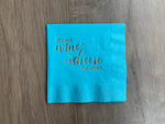 Bright blue cocktail napkin on a grayish wood background. Metallic gold foil print that reads - Let's have wine and cheese for dinner! Design by Stationare