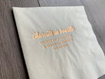 Angled image of an ivory cocktail napkin with metallic gold foil that reads - Charcuterie Boards: where self-control and good intentions go to die. The napkin is against a grayish wooden background. By Stationare.