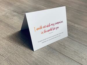A folded white notecard is folded and propped up on a gray wooden background. The card says, "I would not wish any companion in the world but you. To many more fun days & adventures together! Happiest of Valentine's Days to you..." Historic Love collection by Stationare.