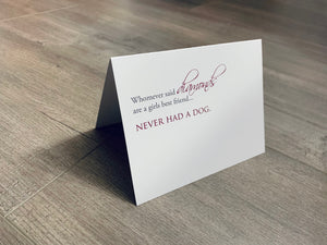 A white, folded notecard sits on a wooden floor. The card says, "Whomever said diamonds are a girls best friend... never had a dog." Dog Lovers collection by Stationare.