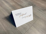 A white, folded notecard sits on a wooden floor. The card says, "All problems can be solved with a good friend and a strong pot of coffee." Coffee Lovers collection by Stationare.