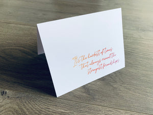 A white, folded notecard sits on a wooden floor. The card says, "It's the hardest of times that always reveal the strongest friendships." The Friendship collection by Stationare.