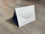 A white folded notecard is propped up on a gray wooden background. In green script printing, the card reads, "Those we love can never be more than a thought away. As long as we cherish a memory with them, they'll find a place in our hearts and there they'll stay." In Sympathy Collection by Stationare.