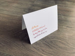 A white, folded notecard is propped up on a gray wooden floor. It reads, "As they say... if at first you don't succeed, try doing it the way your Mom suggested from the beginning." Mother's Day card by Stationare.