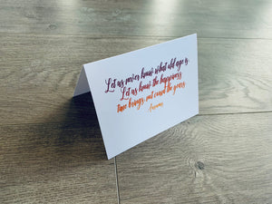A white card is propped on a gray wood floor. The card reads, "Let us never know what old age is. Let us know the happiness time brings, not count the years." Birthday Inspirations by Stationare.