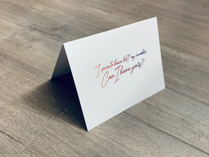 A folded white notecard is propped up on a wooden floor. The card reads, "I seem to have lost my number. Can I have yours?" Stationare's Pick Up Lines collection.