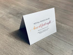 A folded white notecard is folded and propped up on a gray wooden background. The card says, "Not all things can be love at first sight. Not all things are food. Wishing you love, laughs and your favorite indulgences this Valentine's Day!" Valentine Smiles collection by Stationare.