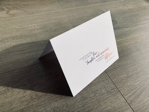 A white card is propped on a gray wood floor. The card reads, "to another year filled with love, laughter and memories that are sure to last a lifetime! happy birthday!" birthday card by Stationare
