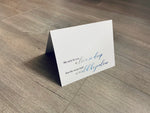 A white card is propped on a gray wood floor. The card reads, "We wish for you a love so deep that the ocean itself would be jealous." Beach Love Collection by Stationare.