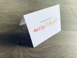 A white, folded notecard sits on a wooden floor. The card says, "let all your days be merry and bright." Christmas Magic collection by Stationare.