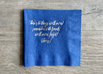 A royal blue napkin lies on a wooden backdrop. In reads, "here's to things we'll never remember with friends we'll never forget! cheers!" in a script silver foil.