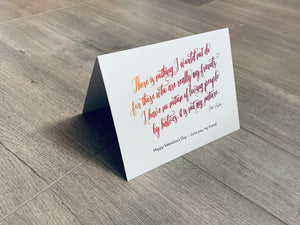 A white, folded notecard sits on a wooden floor. The card has a quote by Jane Austen and says, "There is nothing I would not do for those who are really my friends. I have no notion of loving people by halves, it is not my nature." The Friendship Valentines collection by Stationare.