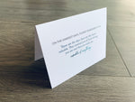 A white, folded notecard sits on a gray wooden floor. The card reads, "On the hardest days, please remember this: These are the days that are the most valuable. They remind you of how strong you are and that you truly are capable of anything." 