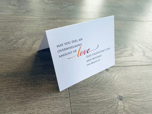 A folded white notecard is folded and propped up on a gray wooden background. The card says, "May you feel an overwhelming amount of love this Valentine's Day and beyond. You deserve it!" VDay BFFs collection by Stationare.