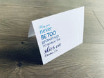 A white, folded notecard sits on a wooden floor. The card says, "May you never be too grown-up to search the skies on Christmas Eve." Christmas Magic collection by Stationare.