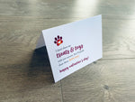 A folded white notecard is folded and propped up on a gray wooden background. The card says, "I don't share my treats and toys with just anyone, but I'd gladly share them with you. Happy Valentine's Day!" Valentines from the Pup collection by Stationare.