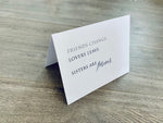 A folded white notecard is propped up on a wooden floor. The card reads, "Friends change. Lovers leave. Sisters are forever." Stationare's Sisters collection.