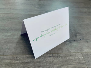 A white folded notecard sits on a gray wood floor. It reads, "You'll never plow a field by turning it over in your mind." Irish Inspirations collection by Stationare.