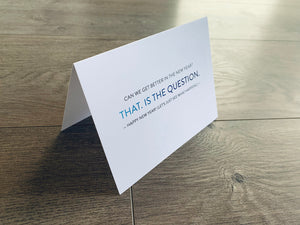 A white folded notecard stands on a gray wood floor. The card reads, "Can we get better in the new year? That. is the question. Happy New Year! Let's just see what happens."