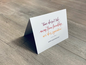 A white, folded notecard sits on a wooden floor. The card has a quote by Tennessee Williams and says, "Time doesn't take away from friendship, nor does separation." The Friendship Valentines collection by Stationare.
