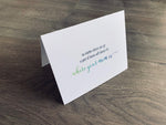 A white folded card is standing up on a wooden floor. The card reads, "no matter where you go a part of home will always be where your mom is." Mother's Day card by Stationare