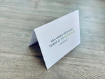 A white folded notecard is propped up on a wooden floor. The card has the Irish proverb, "what whiskey will not cure, there is no cure for." From the Irish Laughs Collection by Stationare.