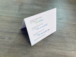 A white, folded notecard sits on a wooden floor. The card says, "Good things come to those who believe better. Better things come to those who are patient. The best things come to those who never give up. Congratulations!" Congrats collection by Stationare.