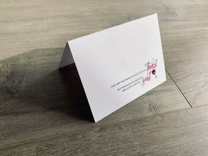 A folded white notecard is propped up on a wooden floor. The card says, "They say that wine is good for the heart but friendships like ours are good for the soul" with a heart inside a wine glass. Stationare's Valen-wine collection.