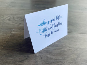 A bright white folded notecard with a get well soon sentiment on the front that reads, "wishing you better health and brighter days to come" in an ombre blue script font. From Stationare's Get Well Soon collection.